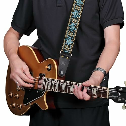 Person playing an electric guitar with a decorative strap.